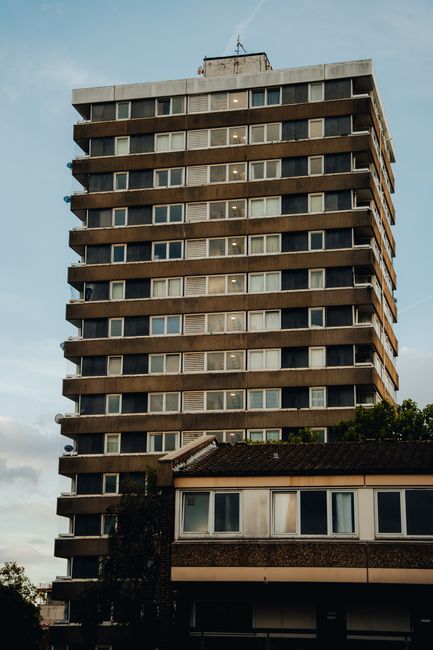 A tall, multi-storey residential building with a rectangular shape, featuring numerous uniform windows arranged in horizontal rows along each floor. The building's exterior is a mix of concrete and da